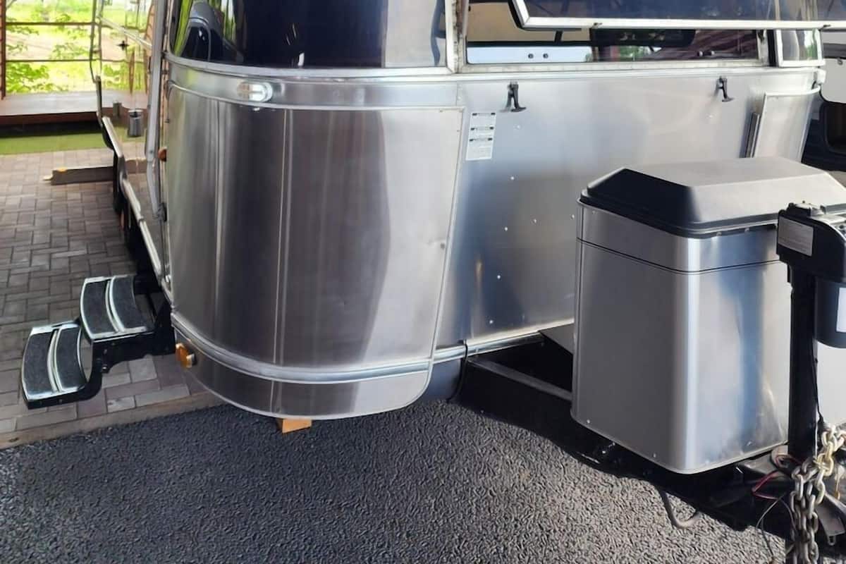 A stationary vehicle with a metallic exterior, labeled 'AIRSTREAM,' parked under a covered area with a roof and metal beams.
