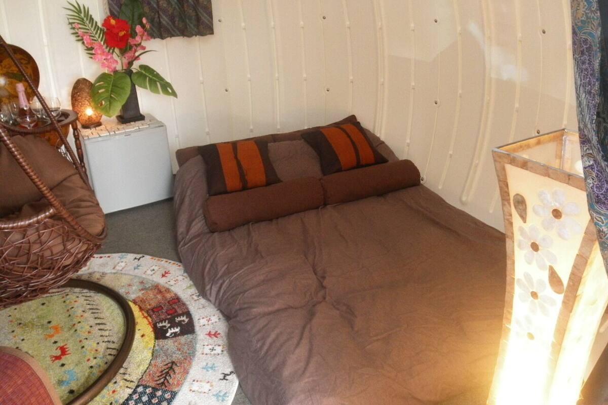A compact room with a bed, a small table, a chair, and a decorative plant.