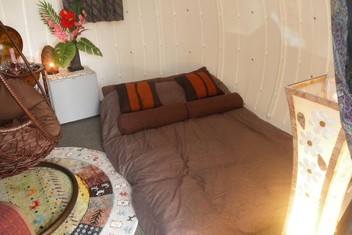 A compact room with a bed, a small table, a chair, and a decorative plant.