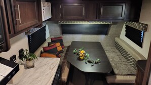 Interior compacto de uma motorhome com área de refeições, assentos, armários e uma cozinha compacta.