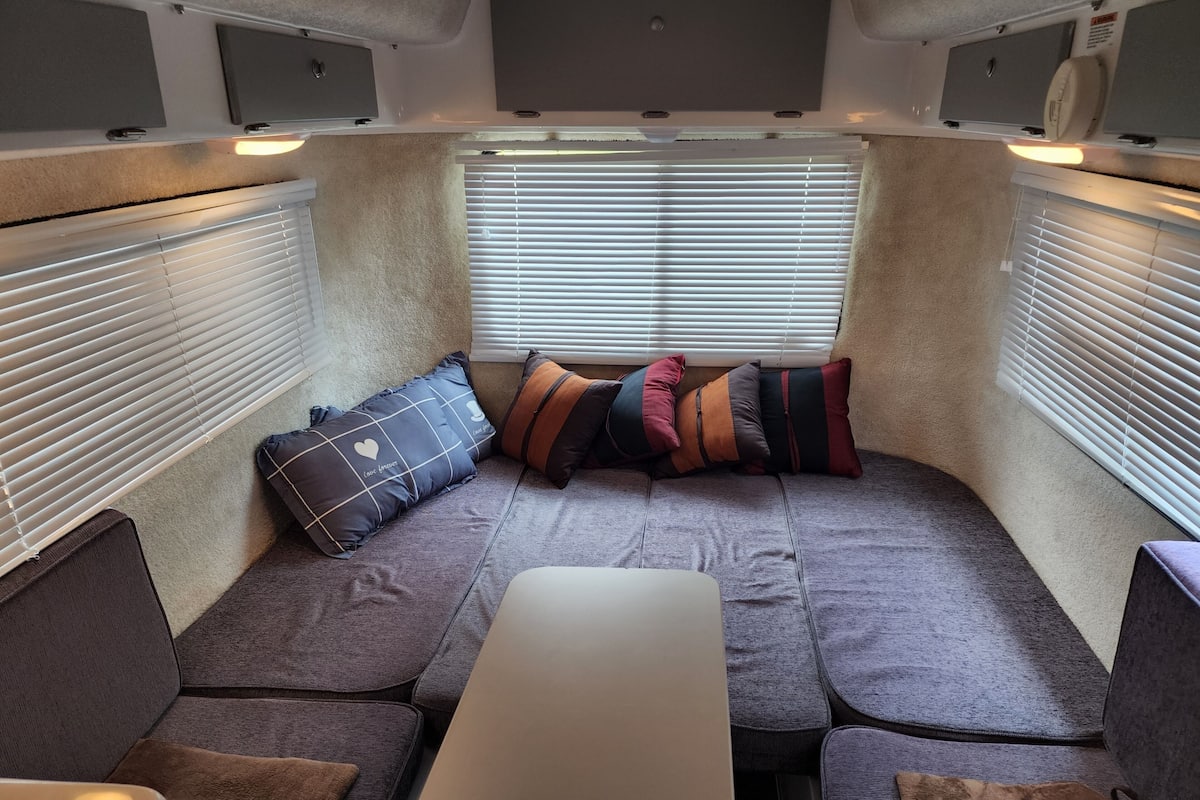 A cozy RV interior with a sectional sofa, a table, and a window with blinds.