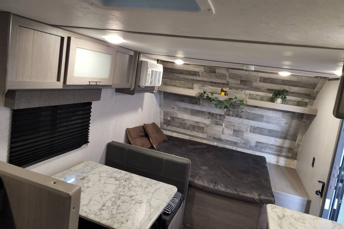 A compact RV interior with a kitchen area, a seating area with cushions, and a built-in shelf with plants.