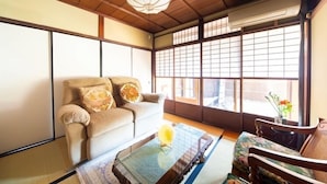 Ett traditionellt japanskt rum med tatamimattor på golvet, en soffa med kuddar, ett glasbord med en dekorativ detalj och utsikt genom shojiskärmar.