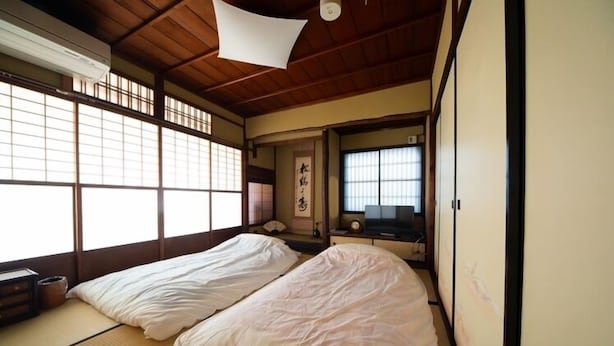 Ett traditionellt japanskt rum med tatamimattor på golvet, två sängar, en shojiskärm och en tv.