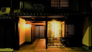 Um edifício japonês tradicional à noite, com entrada bem iluminada, um pequeno jardim de bambu e uma porta deslizante.
