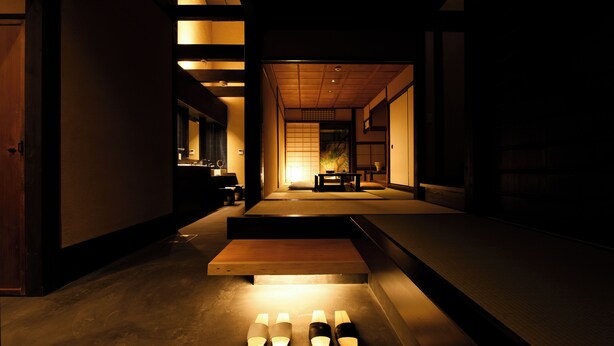 Um interior japonês tradicional com tatames, uma mesa de madeira baixa e uma porta deslizante que dá para um quarto com futon.