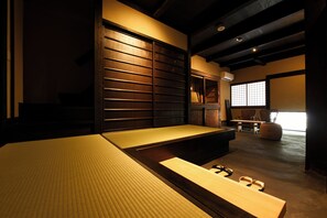 Ein traditioneller Raum mit Tatami-Matten, einer Schiebetür, einem niedrigen Tisch und Blick ins Freie durch ein Fenster.