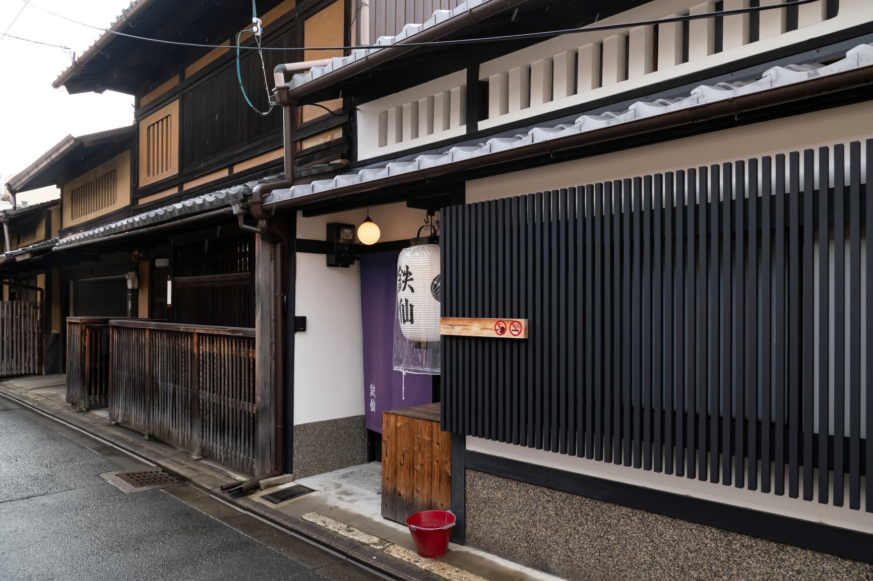 A traditional Japanese building with a wooden entrance, a red bucket, and a sign with Japanese characters.