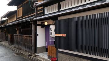 A traditional Japanese building with a wooden entrance, a red bucket, and a sign with Japanese characters.