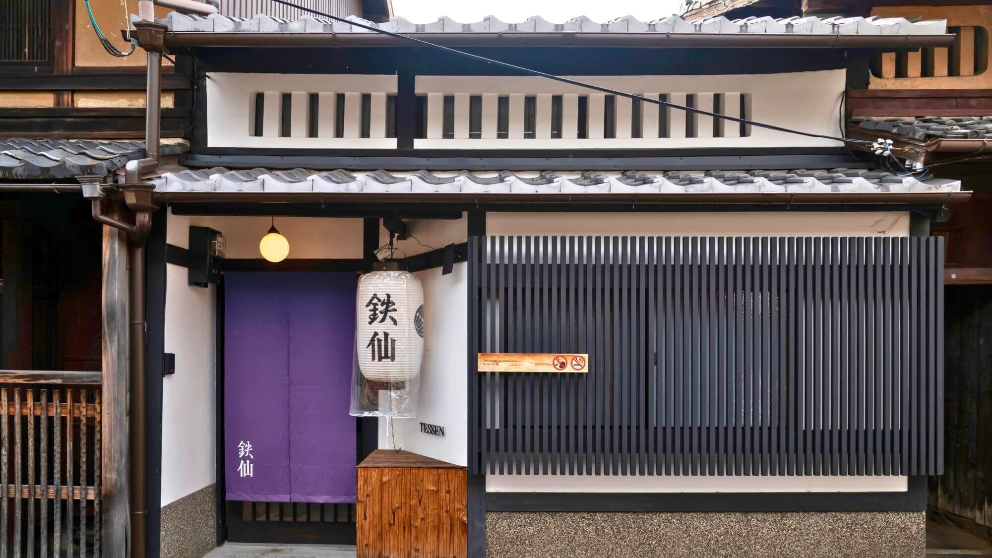 Ein traditionelles japanisches Gebäude mit einer violetten Eingangstür, einem weißen Laternen und einer schwarzen Schiebetür.