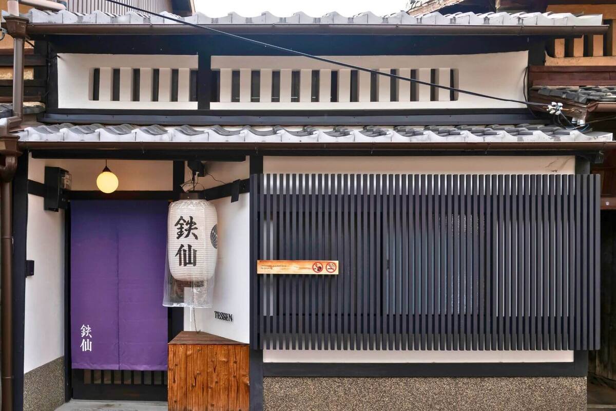 A traditional Japanese building with a purple entrance door, a white lantern, and a black sliding door.