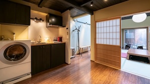A modern kitchen with a washing machine, wooden flooring, and a sliding door leading to a dining area.