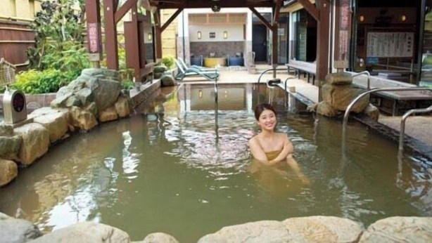A person in a hot spring bath area with stone steps and a wooden structure overhead. - Embellir (Ibaraki)