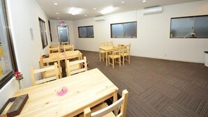 A room with multiple wooden tables and chairs, carpeted floor, and large windows. - Embellir (Ibaraki)