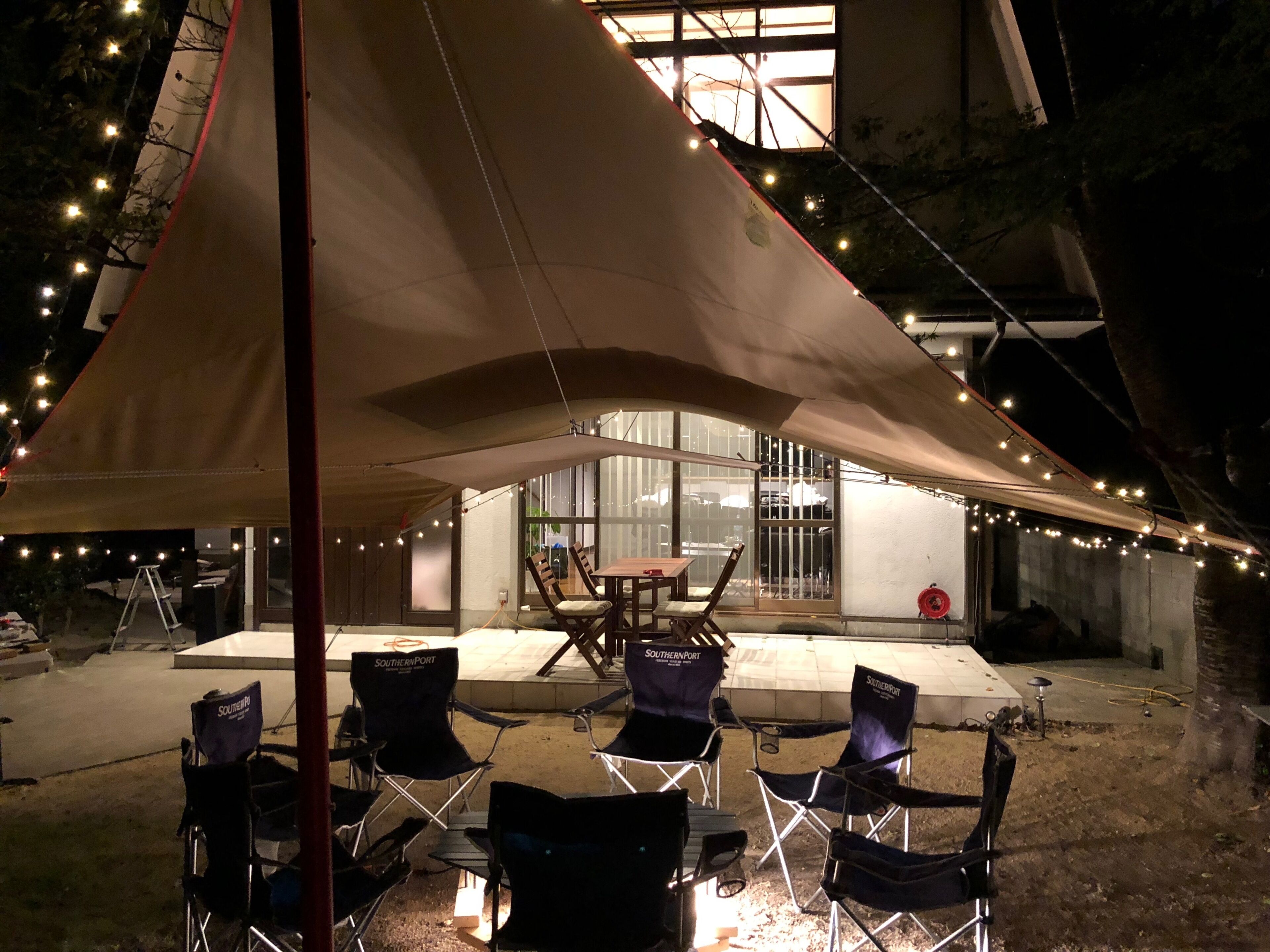 An outdoor seating area with a table and chairs under a canopy, surrounded by string lights.