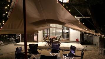An outdoor seating area with a table and chairs under a canopy, surrounded by string lights.