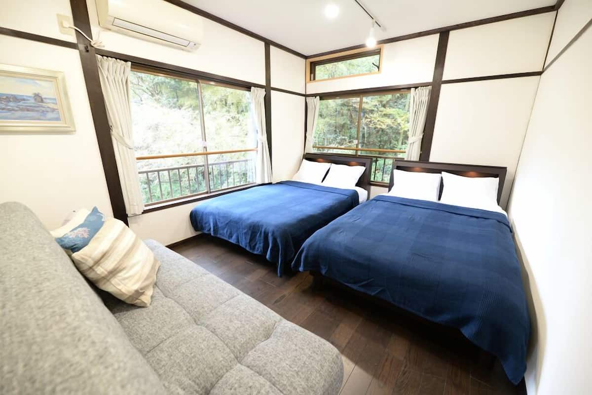 A bedroom with two beds, a sofa, and large windows with curtains.