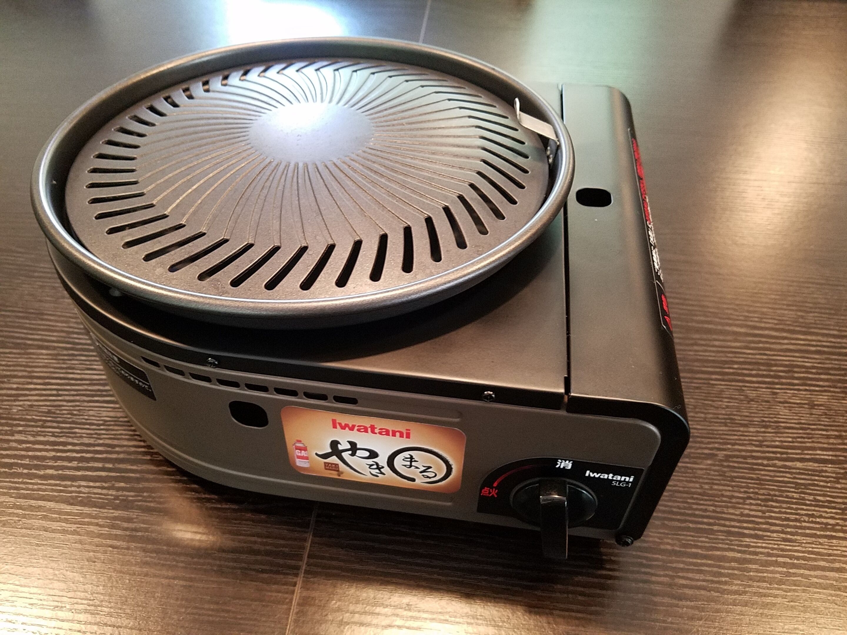 Un barbecue électrique portatif doté d’un bouton de contrôle et d’une étiquette indiquant la marque « Iwatan ».