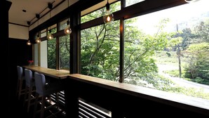 Zona de bar con mostrador de madera y taburetes, ventanas amplias con vistas a zonas verdes.