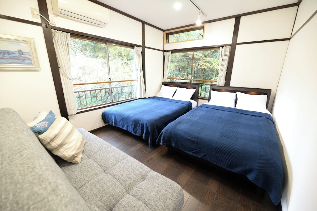 A room with two beds, a sofa, and large windows with curtains.