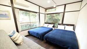 Una habitación con dos camas, un sofá y ventanas amplias con cortinas.