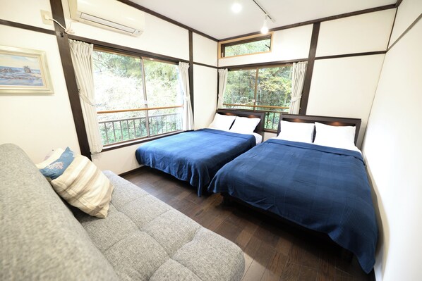 A bedroom with two beds, a sofa, and large windows with curtains.