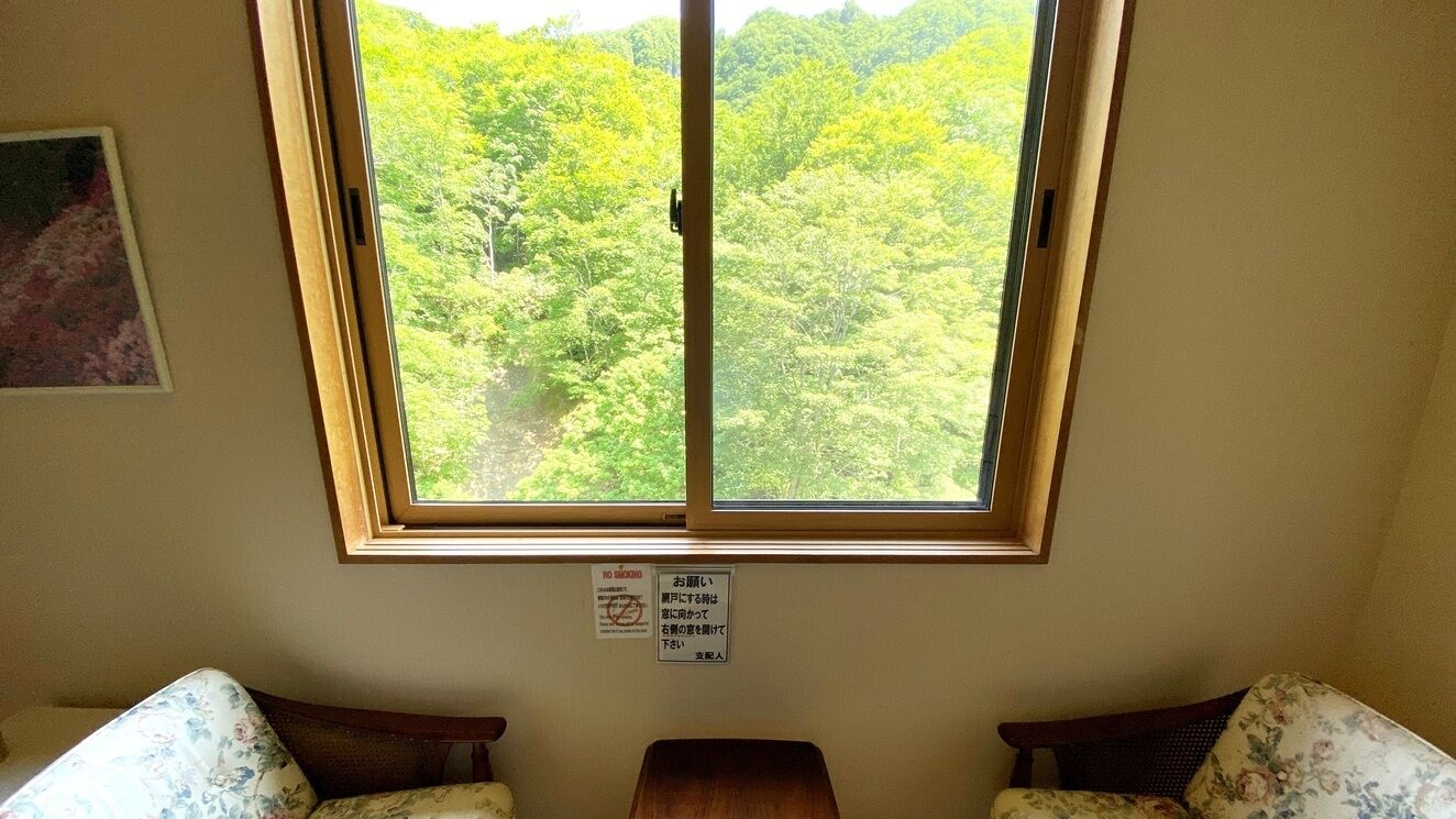 A room with a large window, a wooden table, two floral-patterned sofas, and a framed picture on the wall.