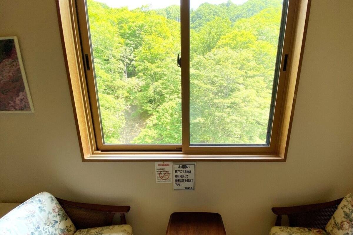 A room with a large window, a wooden table, two floral-patterned sofas, and a framed picture on the wall.