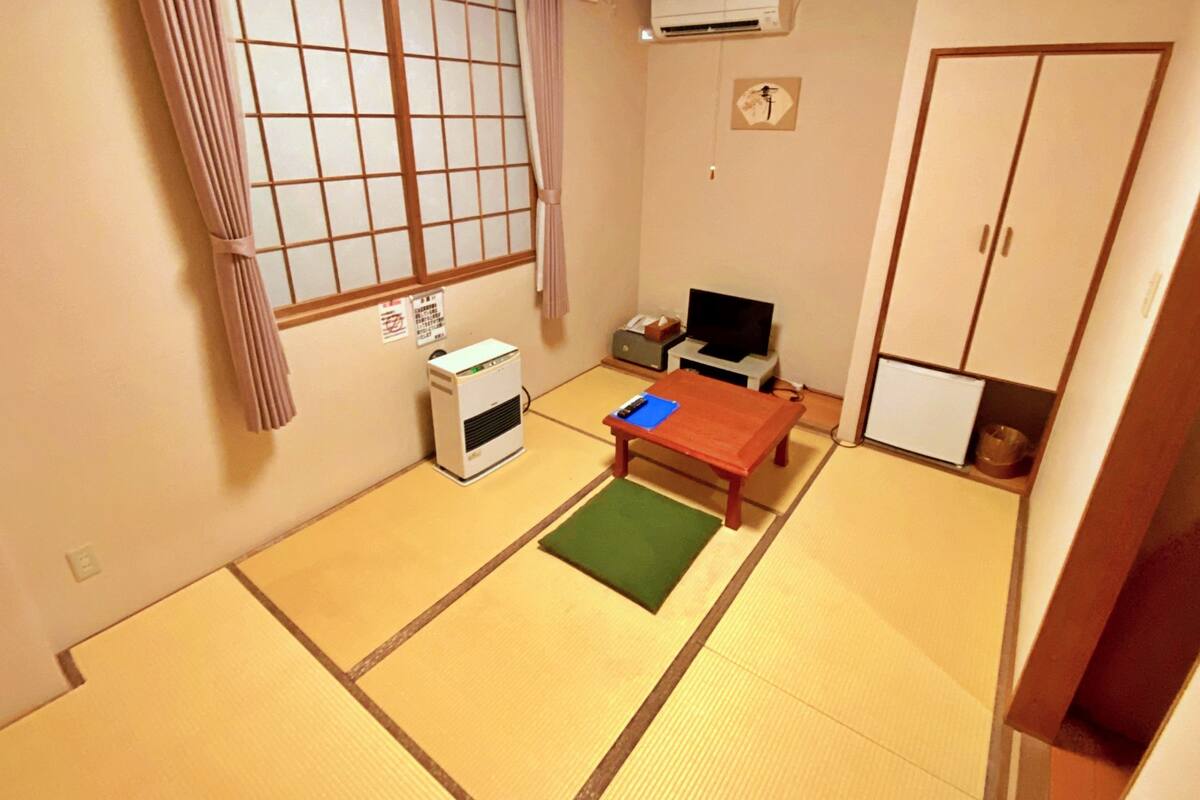 A traditional Japanese room with tatami flooring, a futon bed, a desk with a computer, and a wardrobe.