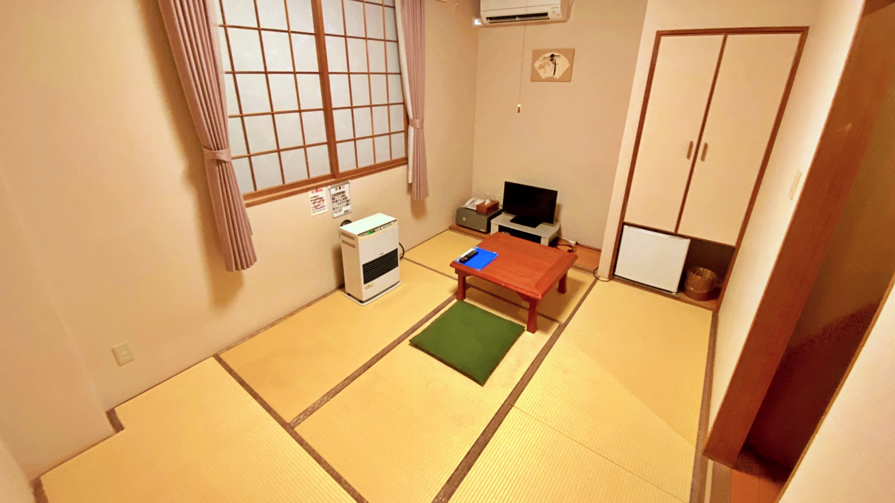 A traditional Japanese room with tatami flooring, a futon bed, a small table, a television, and a wardrobe.