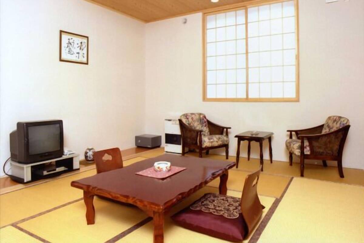 A traditional Japanese room with tatami flooring, a low table, two chairs, a television, and a large window.