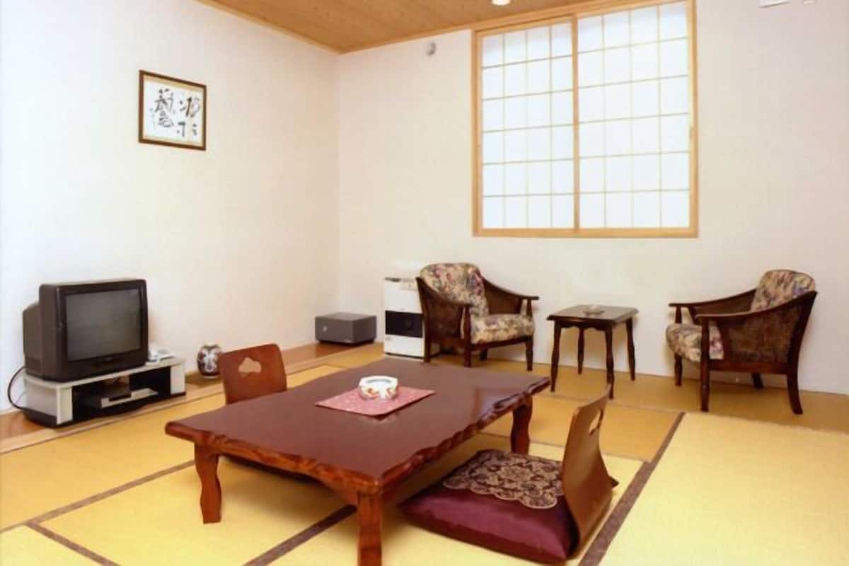 Perinteinen japanilainen huone, jossa on tatamimatto, matala pöytä, kaksi tuolia, televisio ja suuri ikkuna.