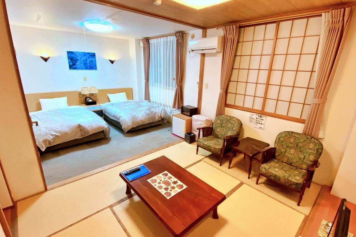 A hotel room with two beds, a sitting area with a table, chairs, and a TV.