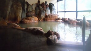 An indoor swimming pool with large rock formations and a view of the outdoors through large windows. - Obokoso (Yakumo)