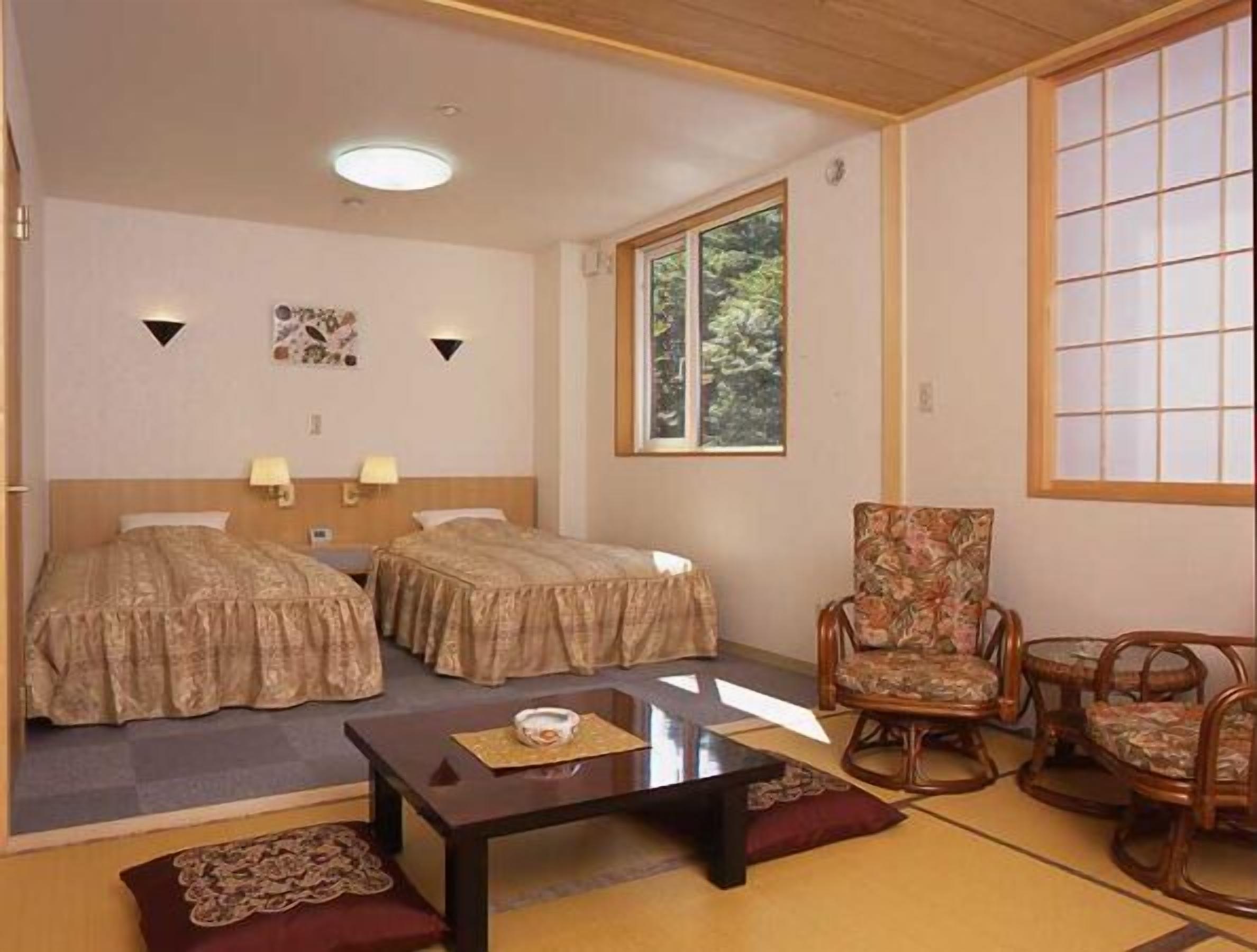 A hotel room with two beds, a small table, a chair, and a window.