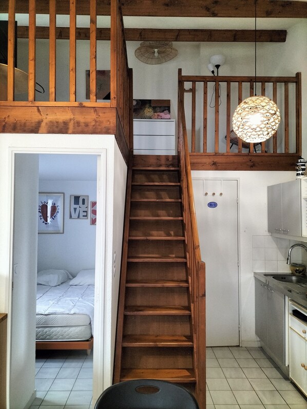 A wooden staircase leading to a loft bedroom with a bed, a small kitchenette, and a ceiling fan. - Le Petit coin Cosy 🐶😸accepted with shared heated pool (Saint-Vincent-sur-Jard)