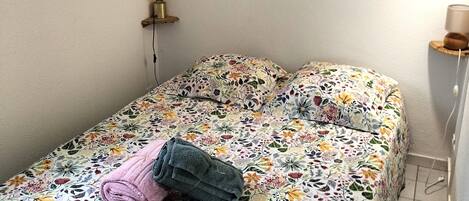 A bedroom with a floral bedspread, a rolled towel, and two framed artworks on the wall.