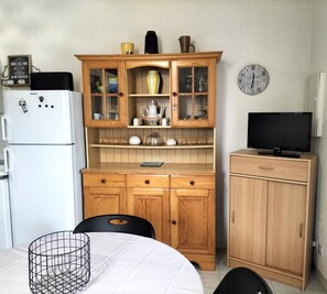 Una cocina compacta con refrigerador, armarios de madera, una mesa de comedor y una televisión.