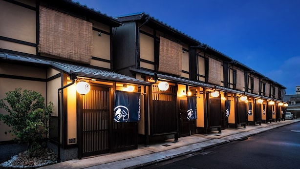 Uma fileira de edifícios em estilo tradicional japonês, com interiores em tatame e uma fileira de lanternas do lado de fora.