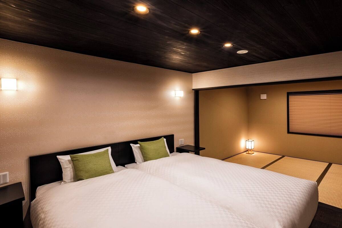 A hotel room with a large bed, bedside tables, wall-mounted lights, and a window with blinds.