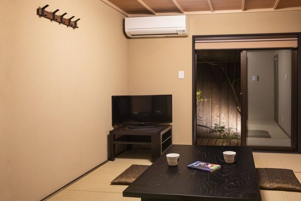 A room with a TV, a table with two cups, a magazine, a sliding door, and a wall-mounted air conditioner.