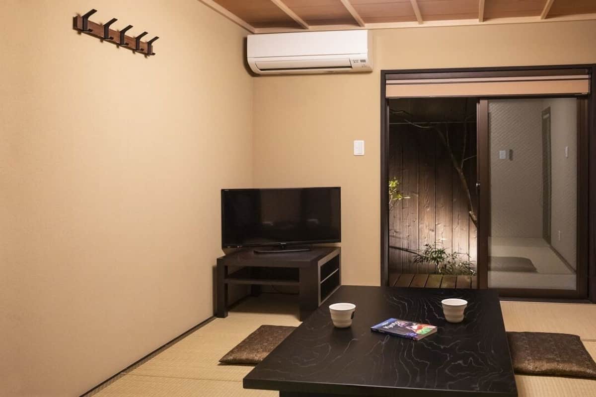 Una habitación con televisión, una mesa con dos tazas, una revista, una puerta corredera y un aire acondicionado instalado en la pared.
