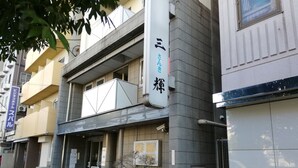 Un edificio con un cartello con su scritto '三輪屋' e una bicicletta parcheggiata fuori.
