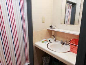 Une salle de bain avec un rideau de douche à rayures, un lavabo avec un miroir au-dessus et un panier rouge posé sur le comptoir.