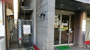 Ingresso di un hotel con cancello in metallo, un cartello che indica ingresso secondario e un tappeto verde all'esterno.