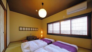 A room with two beds, a small table, a lamp, and a window with a lattice design.