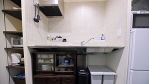 A compact kitchen with white tiled backsplash, a microwave, a kettle, a sink, and a small refrigerator.