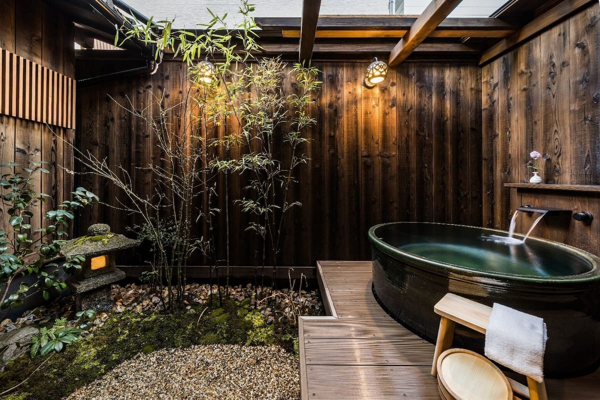 Un espacio de spa de madera con un jacuzzi, un farol de piedra y plantas de bambú.