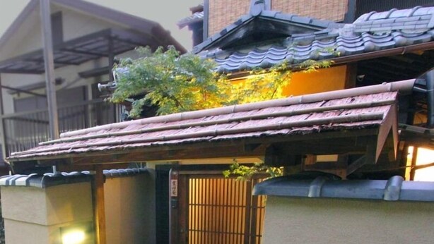 Ein traditionelles japanisches Gebäude mit einem Ziegeldach, einem Holztor und einem kleinen Vordach.