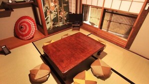 Ein Zimmer mit Tatami-Matten, einem Tatami-Bett, einem Fernseher und einer Schiebetür mit floralem Muster.